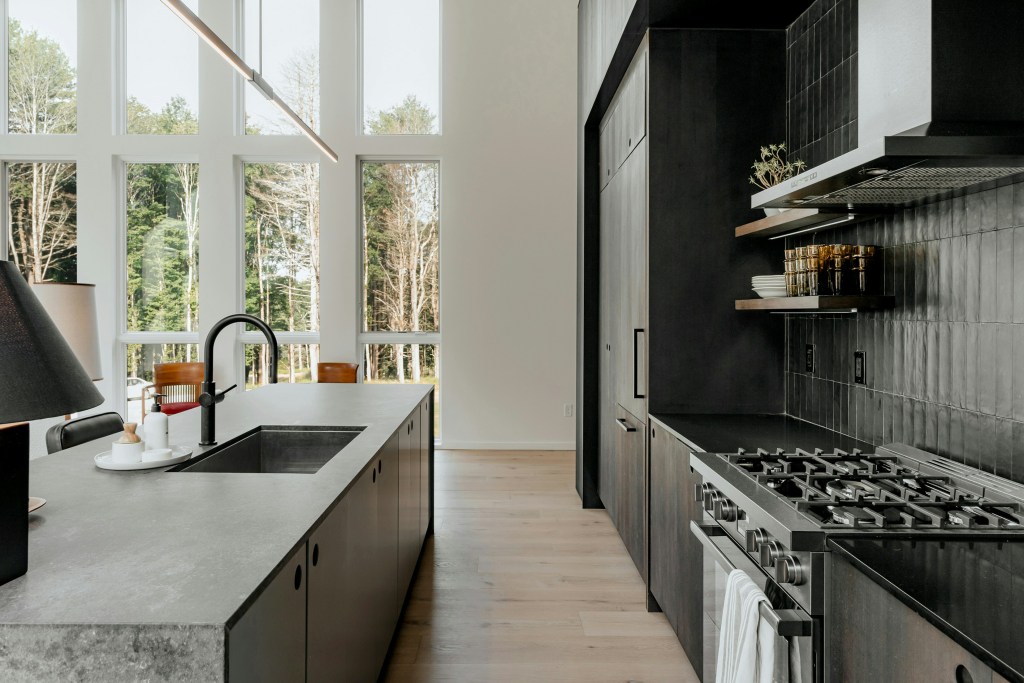 sleek and modern kitchen showing a range and sink and floor to ceiling windows